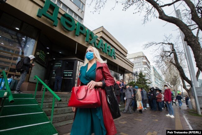 Женщина в маске проходит мимо очереди в аптеку. Алматы, 18 марта 2020 года.